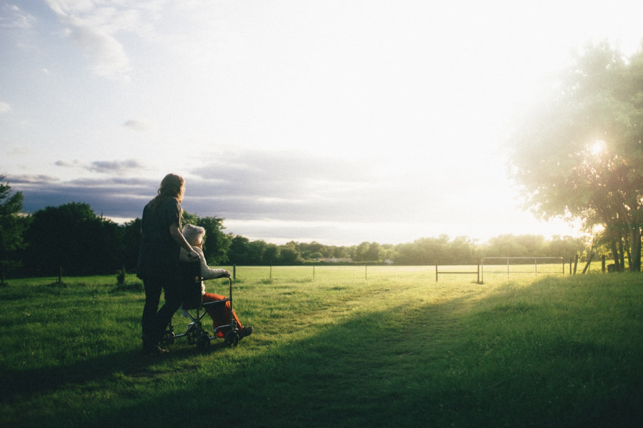 Caregiver walking alongside a senior in a wheelchair at sunset